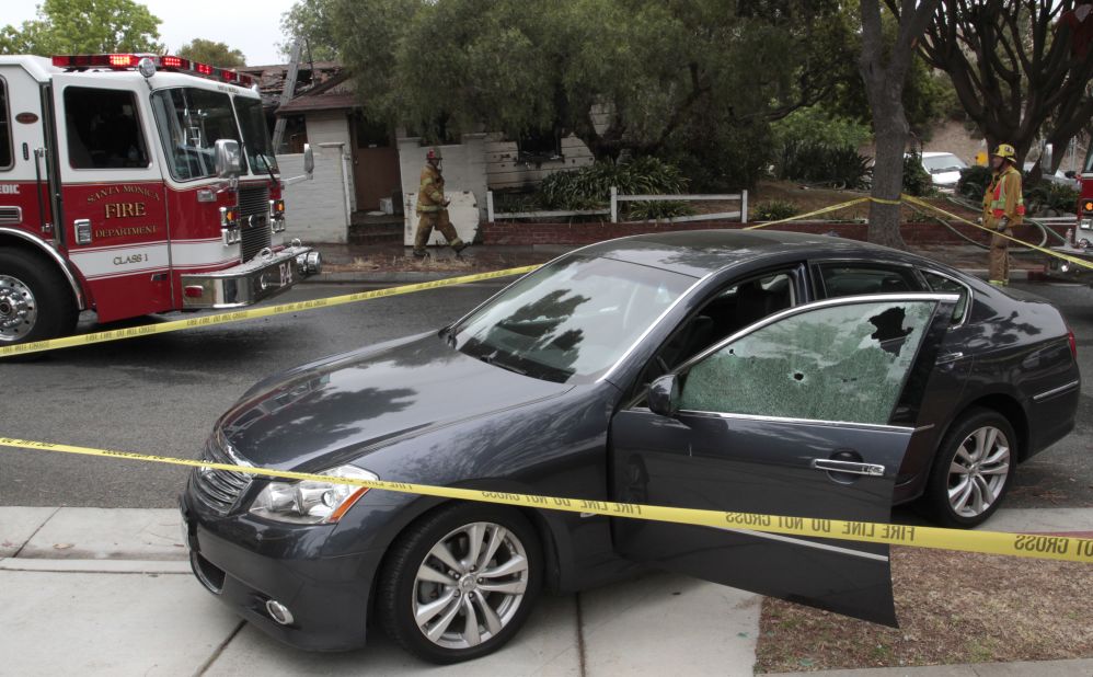 A car with windows shattered by bullets sits in front of a partially burned house where two bodies where found.  Authorities believe the incident may be related to the shooting on the campus of Santa Monica College.