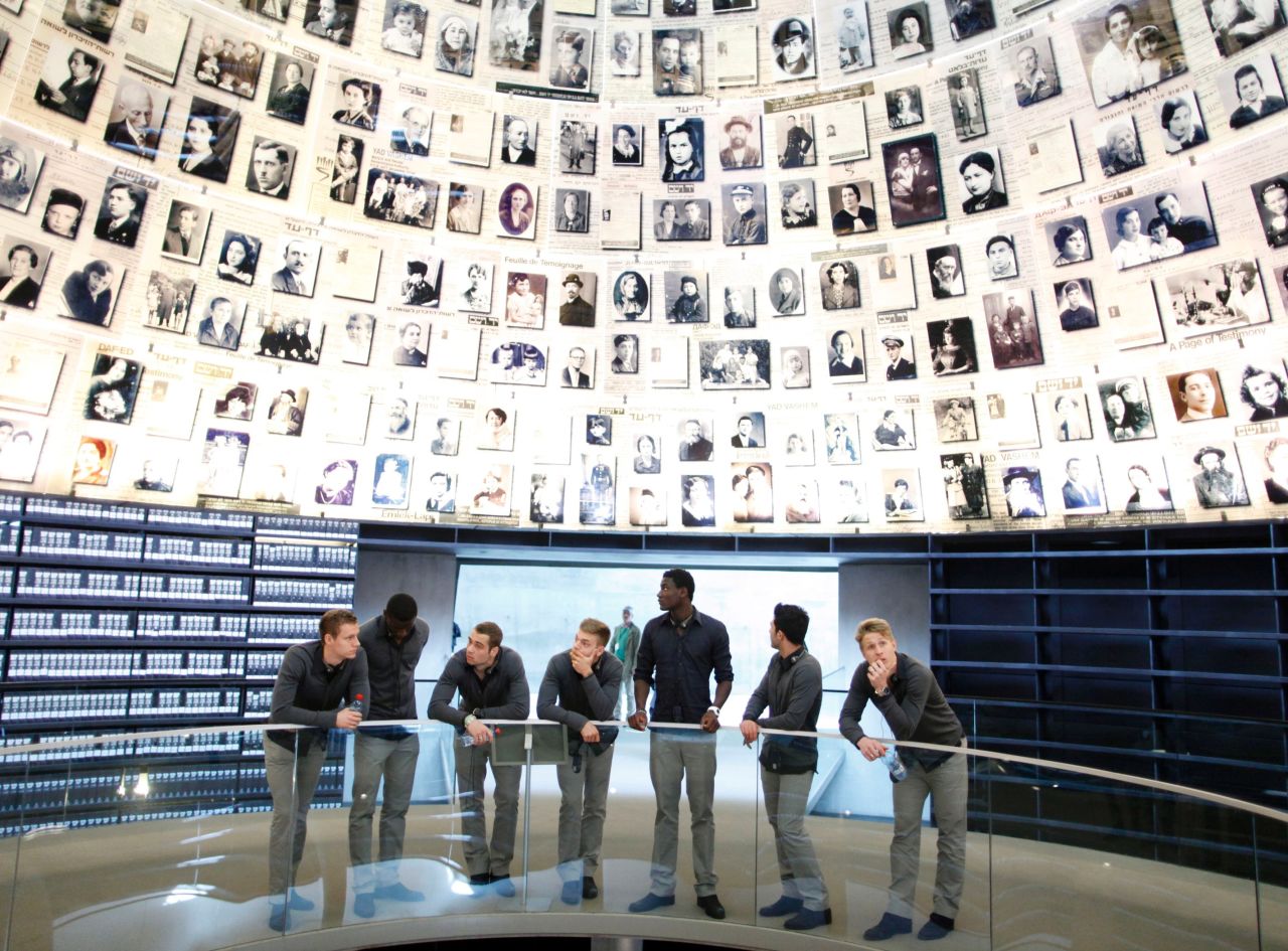 The players take a moment to pause and reflect while surrounded by photos of those who were murdered in the Holocaust.
