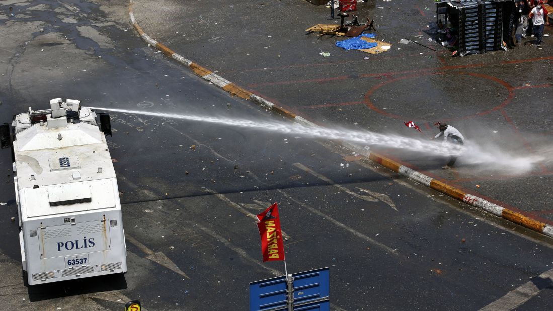 Riot police aim a water cannon at a protester as others take cover behind a makeshift shelter in Taksim Square on June 11.