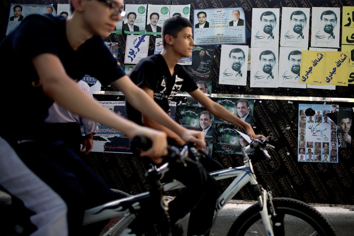 Youths ride past campaign posters in downtown Tehran on Thursday, June 13, a day ahead of the country's presidential election.