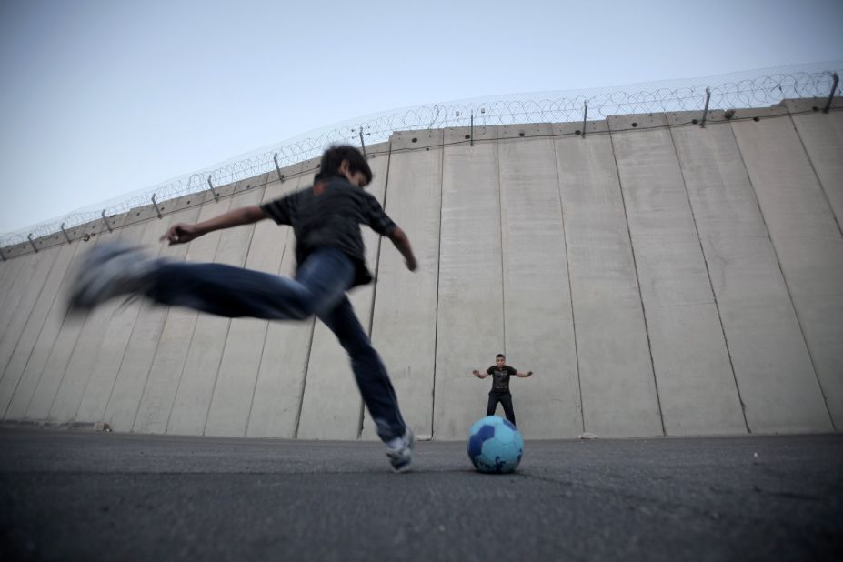 Palestinian children play football in front of the Israeli security fence in the West Bank village of Abu Dis, on the outskirts of Jerusalem.  Organizations such as Mifalot help bring Palestinian and Israeli kids together through the power of football.