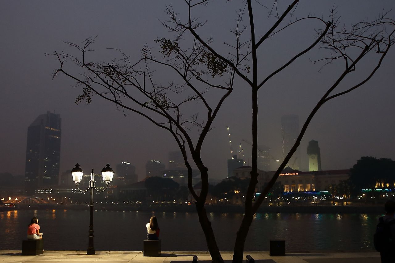 People sat by the Singapore River as the city's hazy skyline was relatively brightened by night lights on June 20.