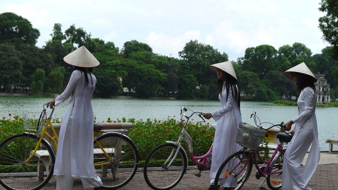 Young girls wear traditional conical hats and "ao dai" dresses in honor of a celebration at Hoan Kiem Lake, a popular hangout for locals.