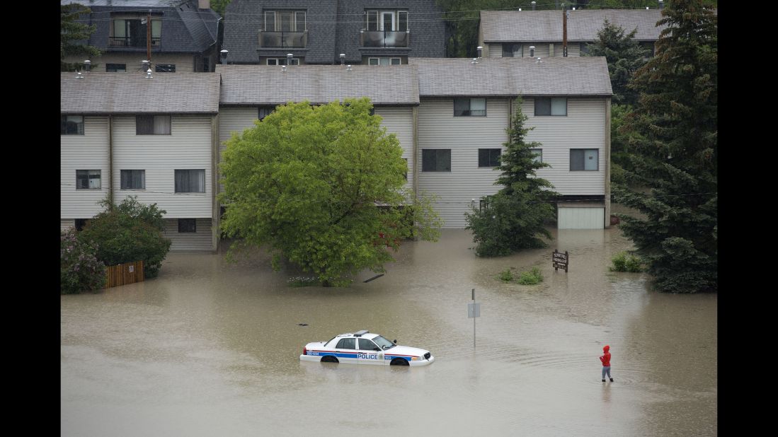 A woman walks toward an abandoned and partially submerged police car in Calgary's Sunnyside neighborhood on June 21. 