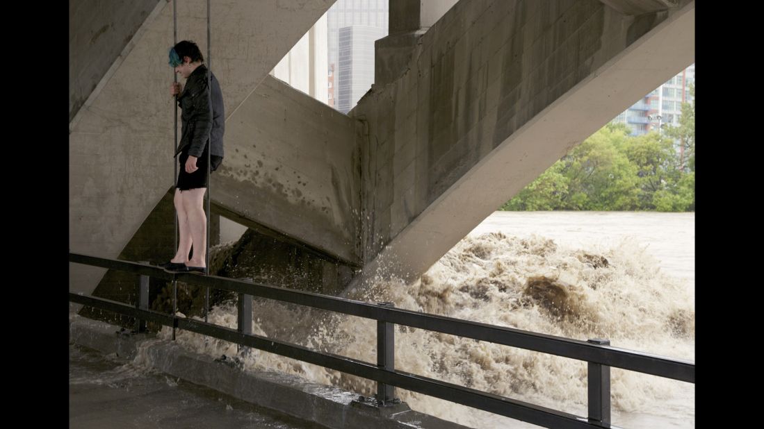 A man stands on a railing under Calgary's Centre Street Bridge as floodwater flows in the background on June 21.