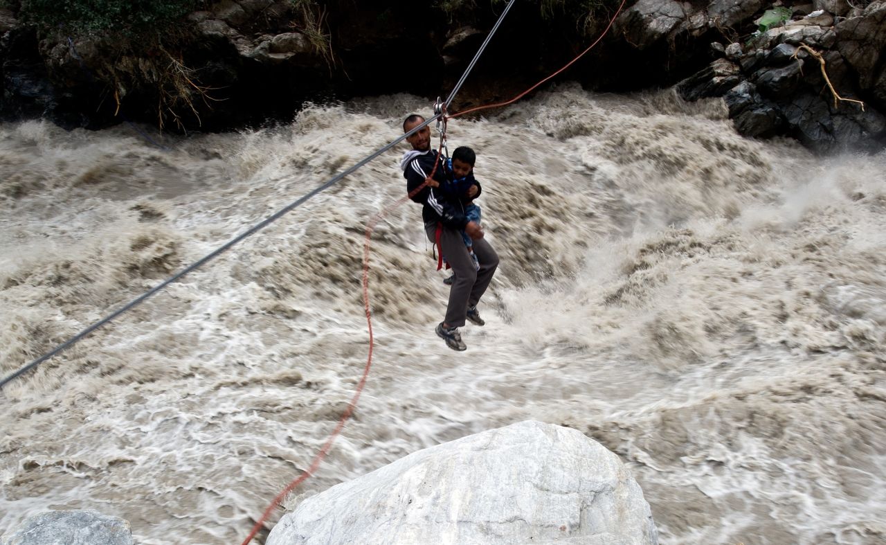 A stranded pilgrim carrying a child is ziplined across a river with the help of Indo-Tibetan Border Police personnel in Govindghat, India, on June 23. 