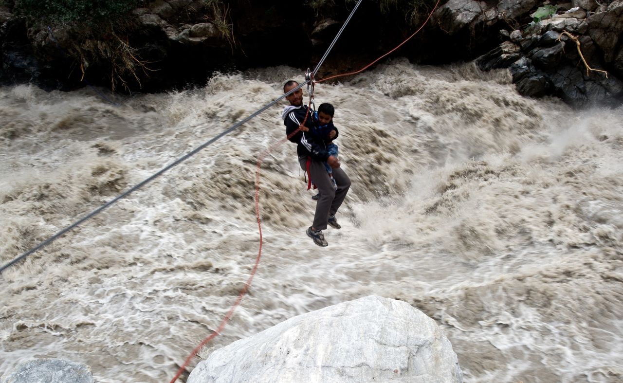 A stranded pilgrim carrying a child is ziplined across a river with the help of Indo-Tibetan Border Police personnel in Govindghat, India, on June 23.
