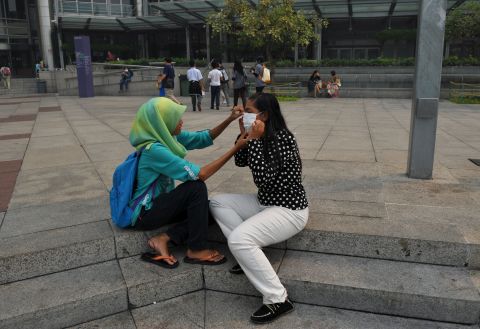 A woman helps her friend with a face mask as haze shrouds Kuala Lumpur on June 23. 