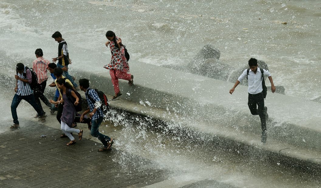 Pedestrians run from water splashing over a sea wall in Mumbai on Monday, June 24.  Authorities are scrambling to rescue thousands of people trapped after floods and landslides ravaged north India, leaving up to 1,000 feared dead. 