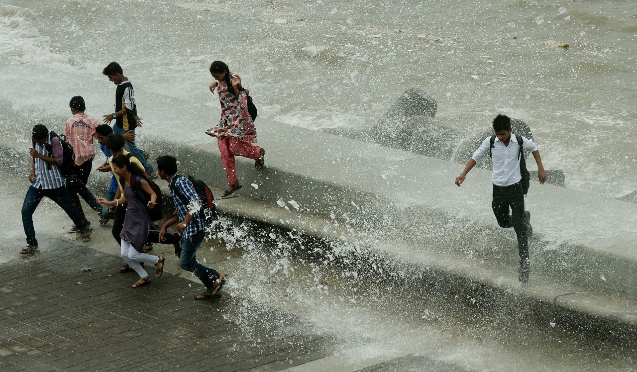 Pedestrians run from water splashing over a sea wall in Mumbai on Monday, June 24. Authorities are scrambling to rescue thousands of people trapped after floods and landslides ravaged north India, leaving up to 1,000 feared dead.