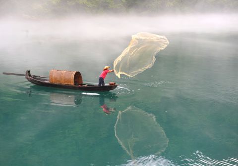A fisherman casts a net on the fog-enveloped Xiaodongjiang River in Zixing, China, on Tuesday, June 25.