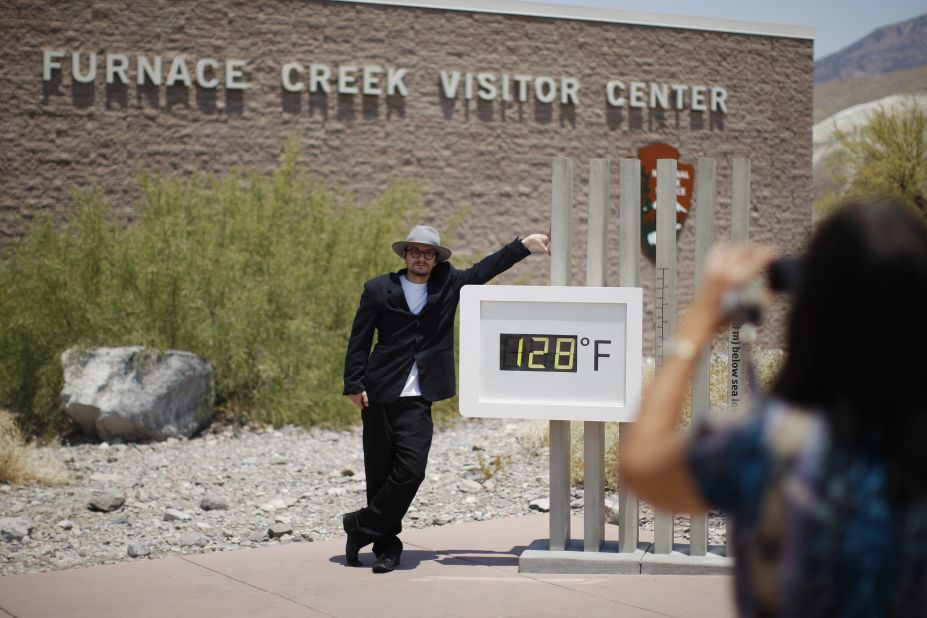 Kevin Martin of Corona, California, poses for a snapshot by an unofficial thermometer at the Furnace Creek Visitor Center in Death Valley National Park on Sunday, June 30. A record-setting and deadly heat wave has spread across the American West. 