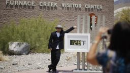 Kevin Martin of Corona, California, poses for a snapshot by an unofficial thermometer at the Furnace Creek Visitor Center in Death Valley National Park on Sunday, June 30. A record-setting and deadly heat wave has spread across the American West. 