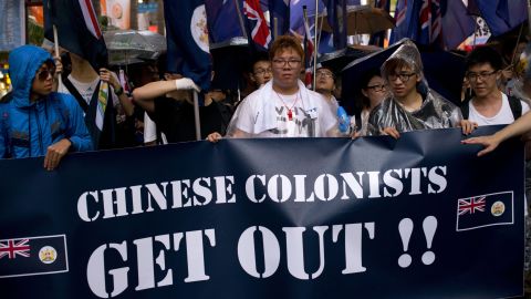 Protesters rallying for democracy on July 1, 2013 carry British-era Hong Kong flags and a banner that reads 'Chinese Colonists Get Out!!'