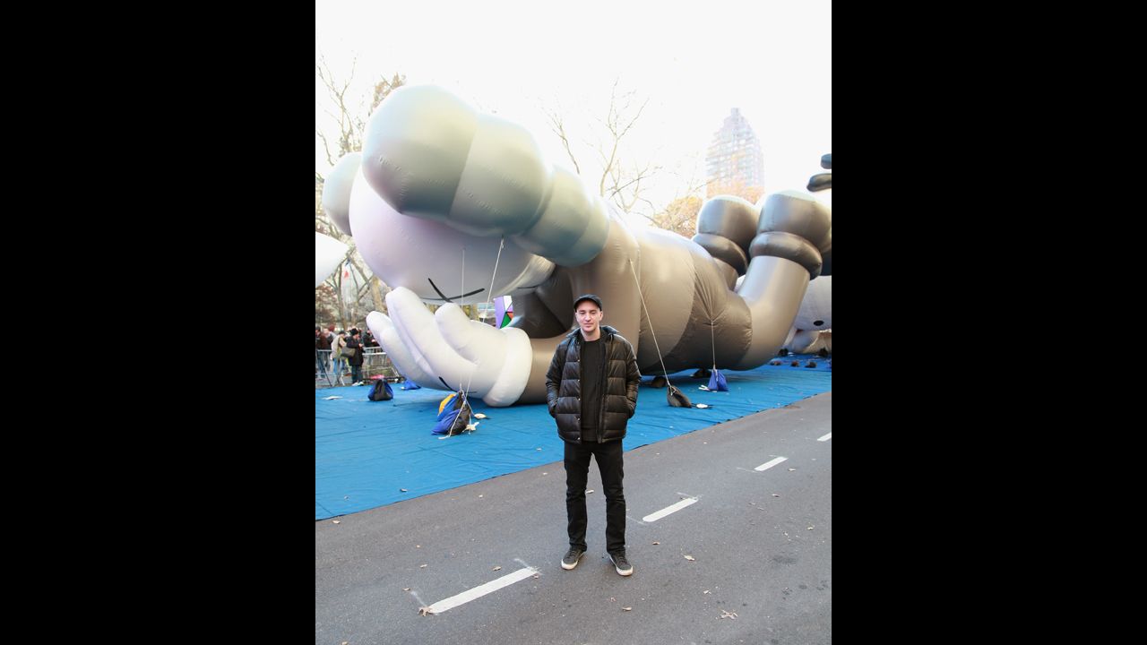 Artist KAWS poses in front of his balloon "Companion" at the 86th Annual Macy's Thanksgiving Day Parade's "Inflation Eve" on November 21, 2012, in New York.