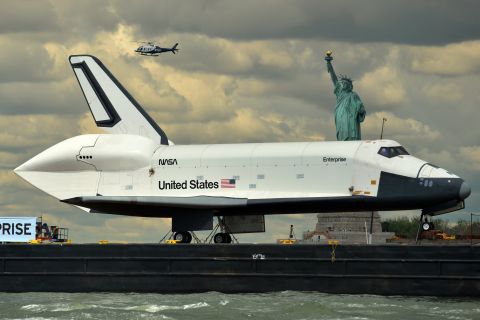The Space Shuttle Enterprise passes the statue while being towed on a barge in June 2012.
