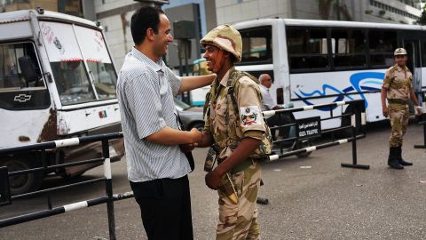 A pedestrian shakes hands with a member of the military at a roadblock in Giza.