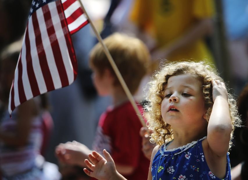 Meriya Merrill, 3, cranes her neck to take in the Independence Day parade in Edina, Minnesota, as her grandmother holds a flag behind her.