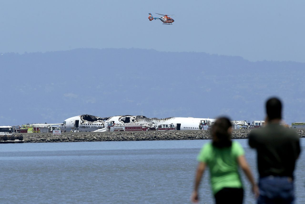 A helicopter flies above the wreckage on July 6 as people observe from across the waters of San Francisco Bay.