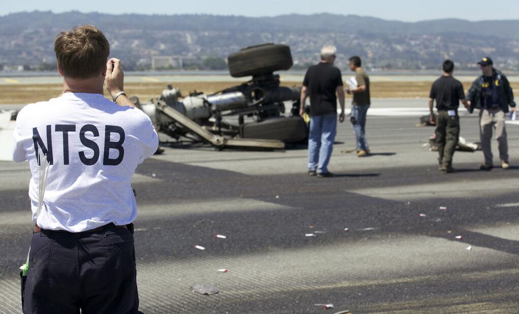 An investigator photographs part of the landing gear at the crash site in a handout released on July 7. Investigators believe that the pilots were flying too slow and too low as they neared the airport on July 6.  