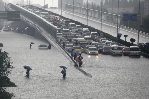 Heavy rains force people to walk across a flooded road and leave vehicles trapped on a viaduct in Wuhan, the capital of Hubei province in central China, on Sunday, July 7. 