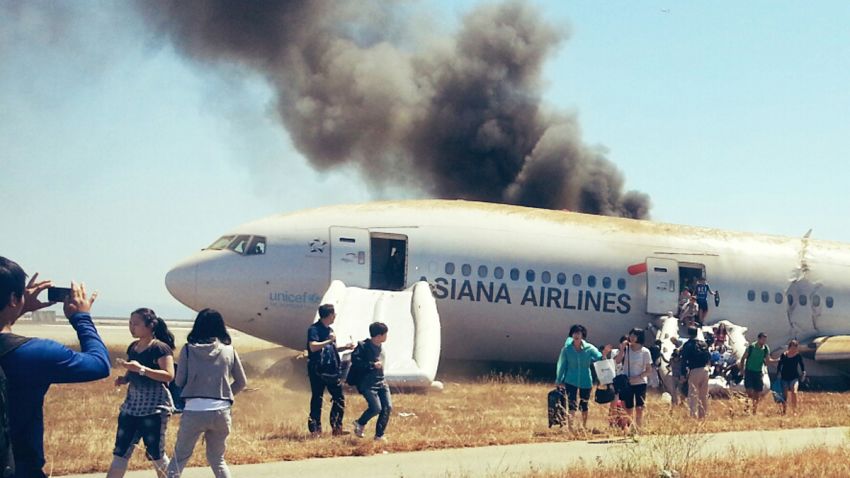 Several passengers escape Asiana Airlines flight 214 with their baggage and stop to take photos of the burning wreckage.