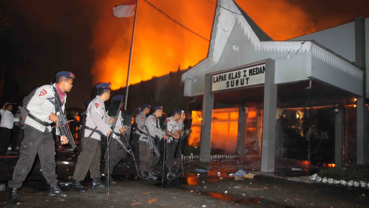 Armed Indonesian police secure the entrance of a burning prison compound in Medan city on July 11, 2013. 