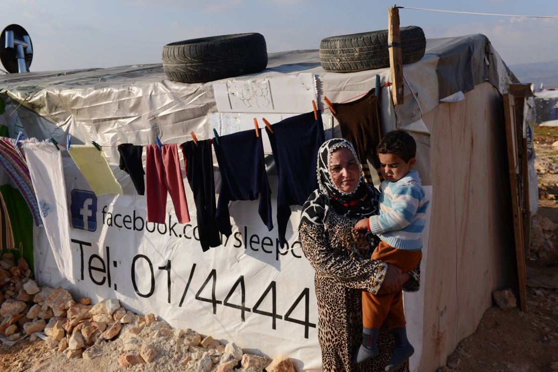 A woman refugee holds her son outside a tent shelter in a makeshift encampment in the Bekaa Valley of Lebanon. 