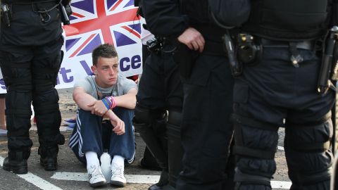 A man sits next to riot police in Belfast on July 13.
