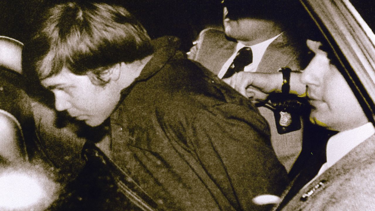 Hinckley is escorted by police following his arrest.  He was obsessed with actress Jodie Foster, haven written to her from his hotel room earlier that day, "There is a definite possibility that I may be killed in my attempt to get Reagan." Hinckley wrote he was doing this to try to win her love.