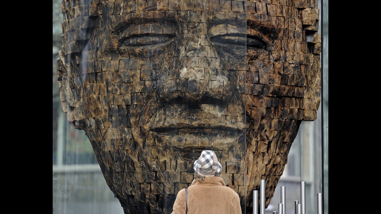 <strong>GERMANY:</strong> A woman views a giant wooden head of Mandela in the city center of Essen in western Germany. Created by artist Jems Robert Koko Bi from the Ivory Coast, the sculpture is made of burned spruce wood and is supposed to stand for the fight for freedom. 