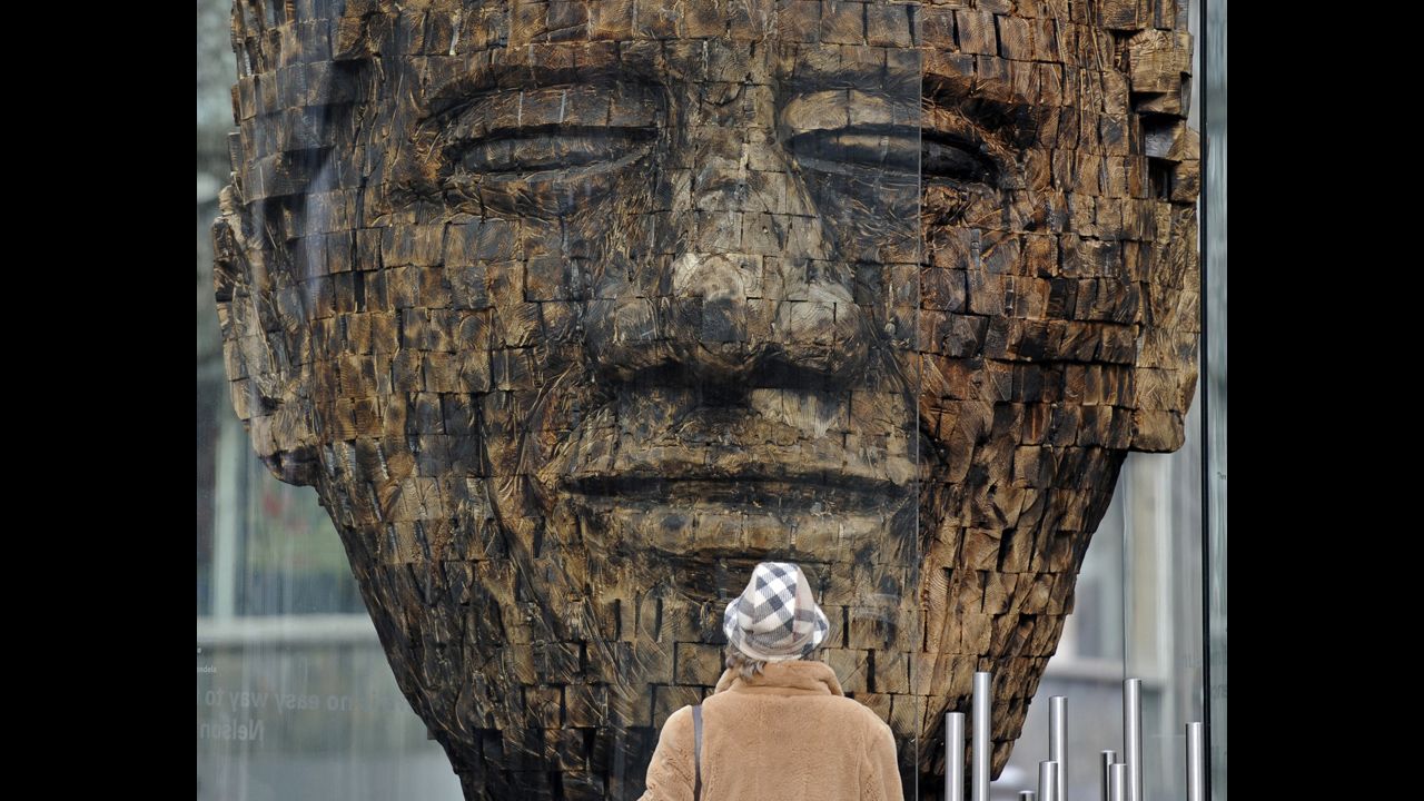 <strong>GERMANY:</strong> A woman views a giant wooden head of Mandela in the city center of Essen in western Germany. Created by artist Jems Robert Koko Bi from the Ivory Coast, the sculpture is made of burned spruce wood and is supposed to stand for the fight for freedom.