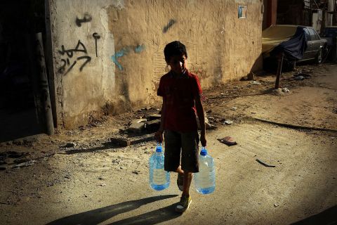 A boy walks with jugs of water in a Beirut neighborhood with a high concentration of Syrian refugees.