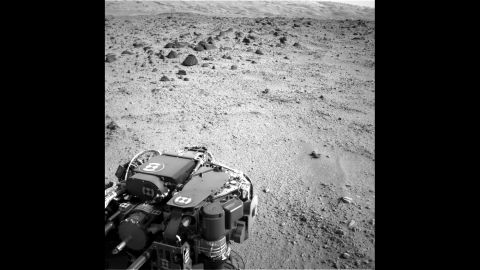 The lower slopes of "Mount Sharp" are visible at the top of this image, taken on July 9, 2013. The turret of tools at the end of the rover's arm, including the rock-sampling drill in the lower left corner, can also be seen. 