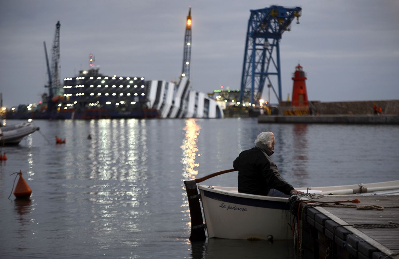 A man sits in his boat in front of the half-submerged cruise ship on January 8, 2013.