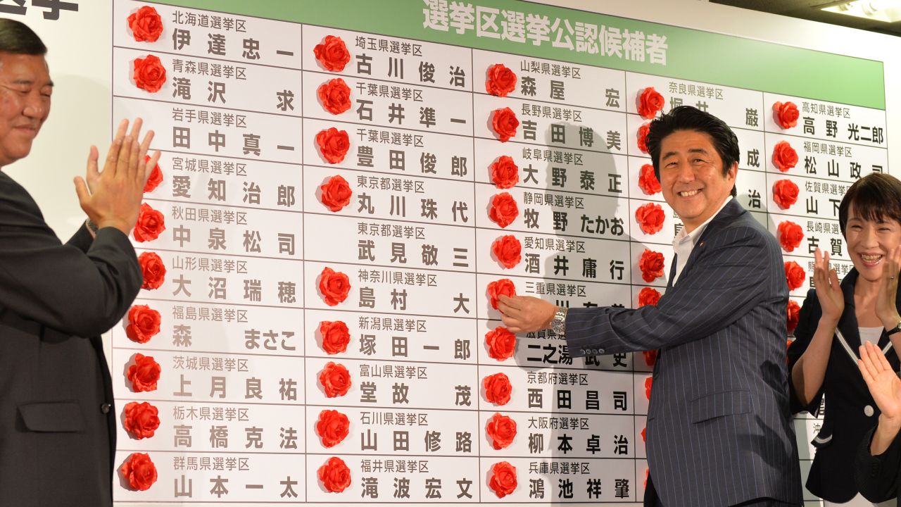 Japan's PM Shinzo Abe smiles as he places a rose on an LDP candidate's name to indicate an election win on July 21, 2013. 