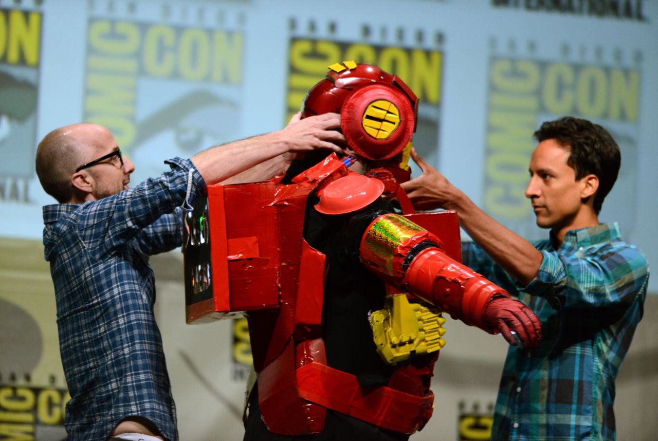 Dan Harmon, center, creator and executive producer of "Community," is helped out of a costume by actors Jim Rash, left, and Danny Pudi during the "Community" panel on the final day of Comic-Con International on Sunday, July 21, in San Diego. Running from Wednesday through Sunday, July 21, the event floods the San Diego Convention Center with more than 100,000 attendees as they shuffle between panels promising exclusive previews and answers to fans' burning questions. <a href="http://www.cnn.com/2013/07/18/us/gallery/comic-con-2013/index.html" target="_blank">See more sights from Comic Con 2013</a>.