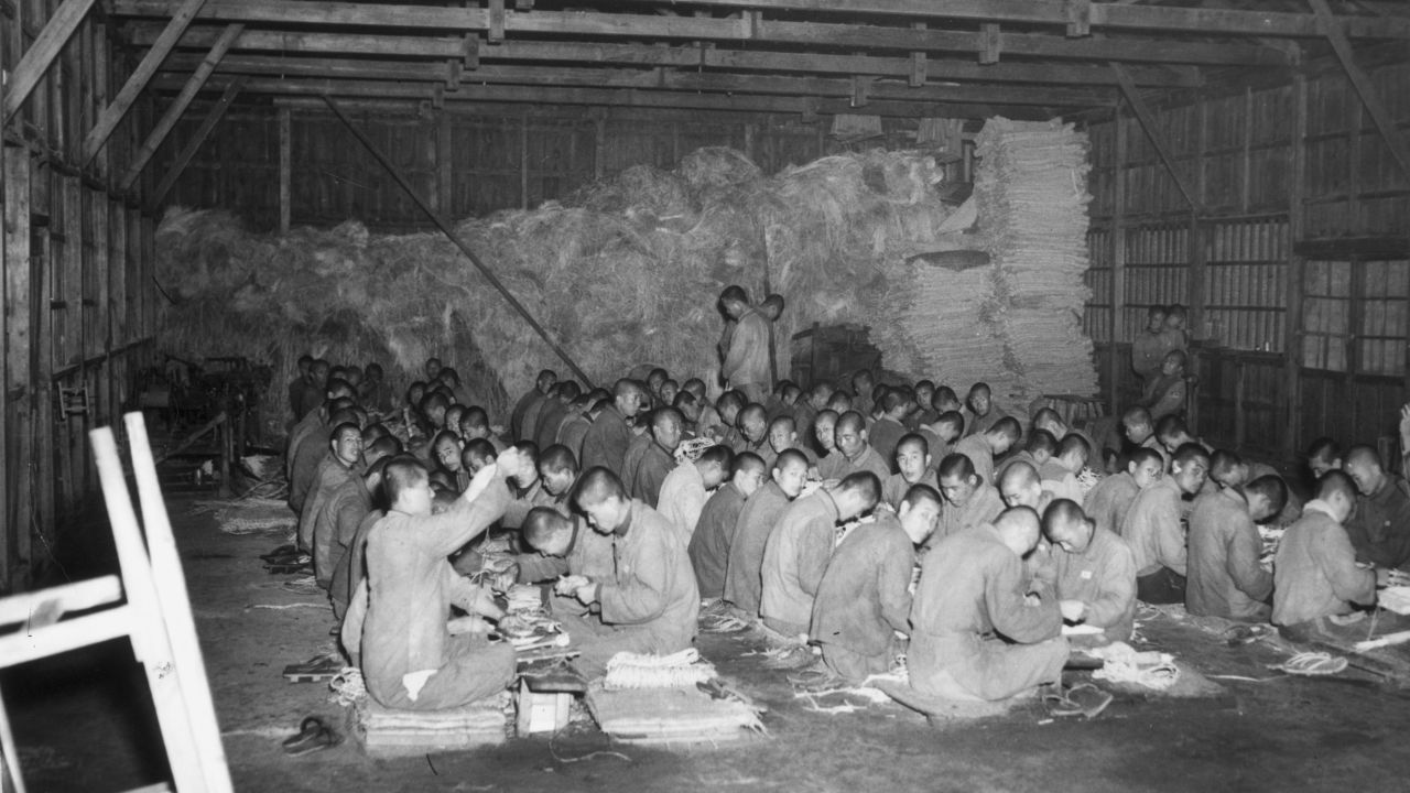 North Korean prisoners of war make baskets on the floor of a storage barn at a prison, circa 1951.