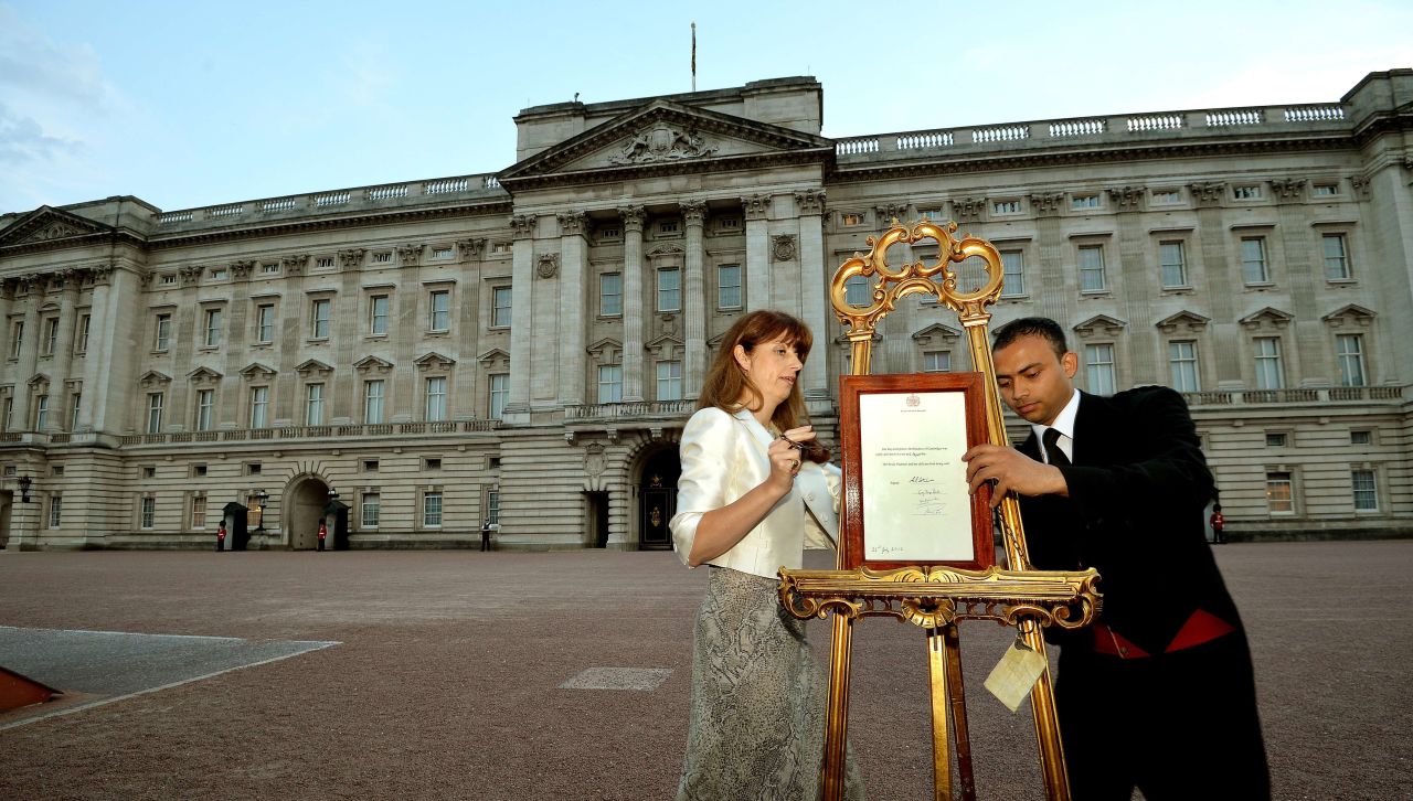 The queen's press secretary, Ailsa Anderson, left, and Badar Azim, a palace footman, place the official birth announcement on a golden easel in front of Buckingham Palace on July 22.