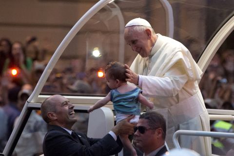 A member of the security detail holds up a baby for Pope Francis to kiss on July 22.