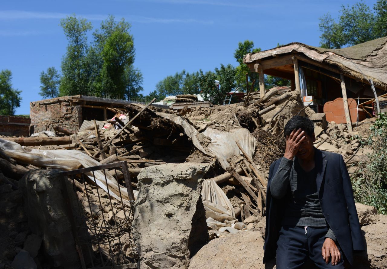 A man sits beside a collapsed house in Gansu province, in northwest China, on July 23.