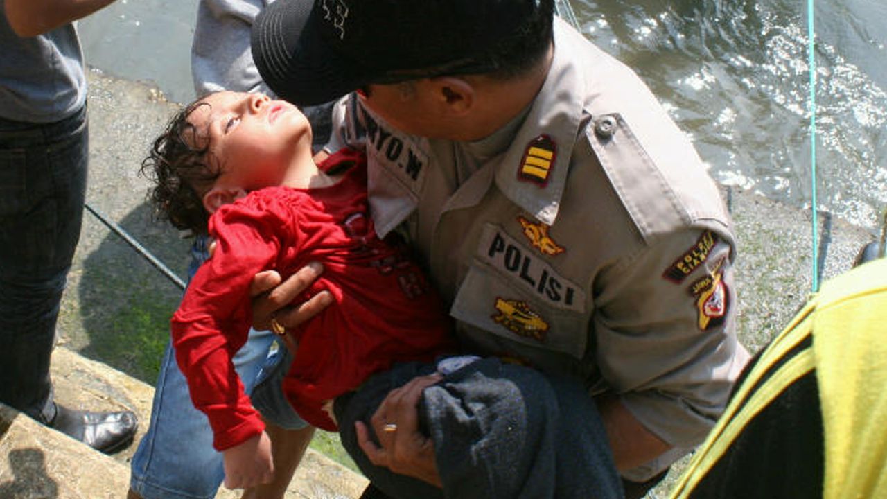 An Indonesian police man carries an exhausted asylum seeker boy rescued from waters off West Java on July 24, 2013. 