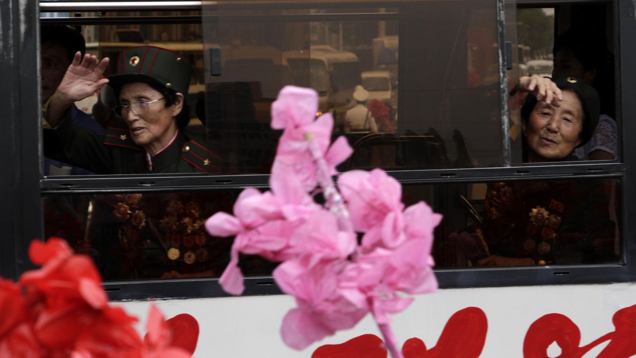 Veterans of the Korean War wave at the crowd as they leave by bus after arriving at the Pyongyang railway station Tuesday, July 23.