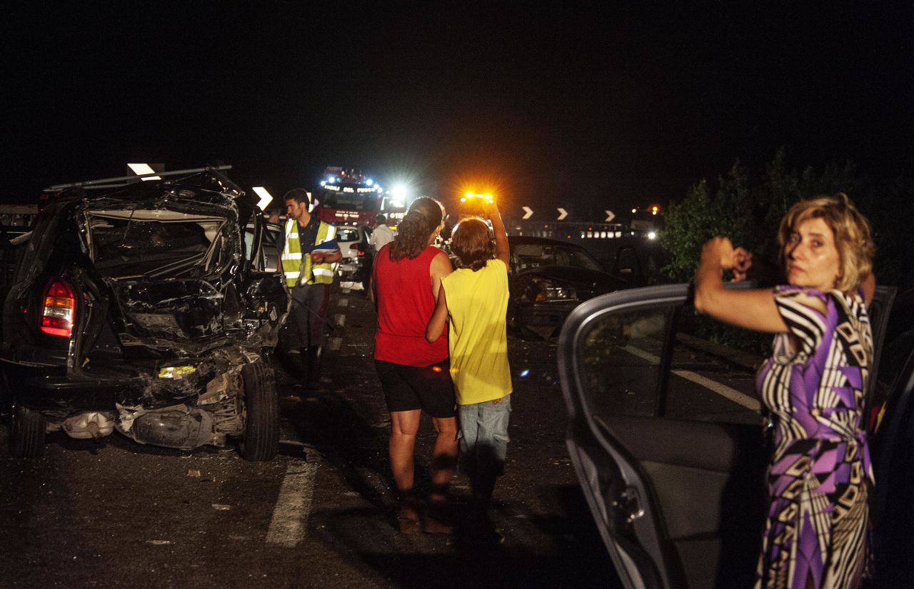 Emergency workers and onlookers stand among damaged cars at the scene of the accident. 