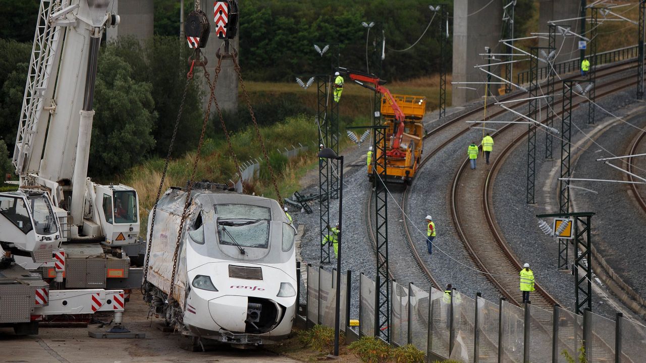 Wreckage of the front locomotive of a derailed train stands on the road while workers repair the railway on Sunday, July 28, in Santiago de Compostela, Spain. A spokeswoman for the Galician regional government said that at least 79 people were confirmed dead in the train crash. It occurred on the eve of a public holiday, when more people than usual may have been traveling in the region.