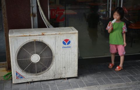 A young girl in Shanghai eats a popsicle next to an air conditioning unit to cool off on Tuesday, July 16.