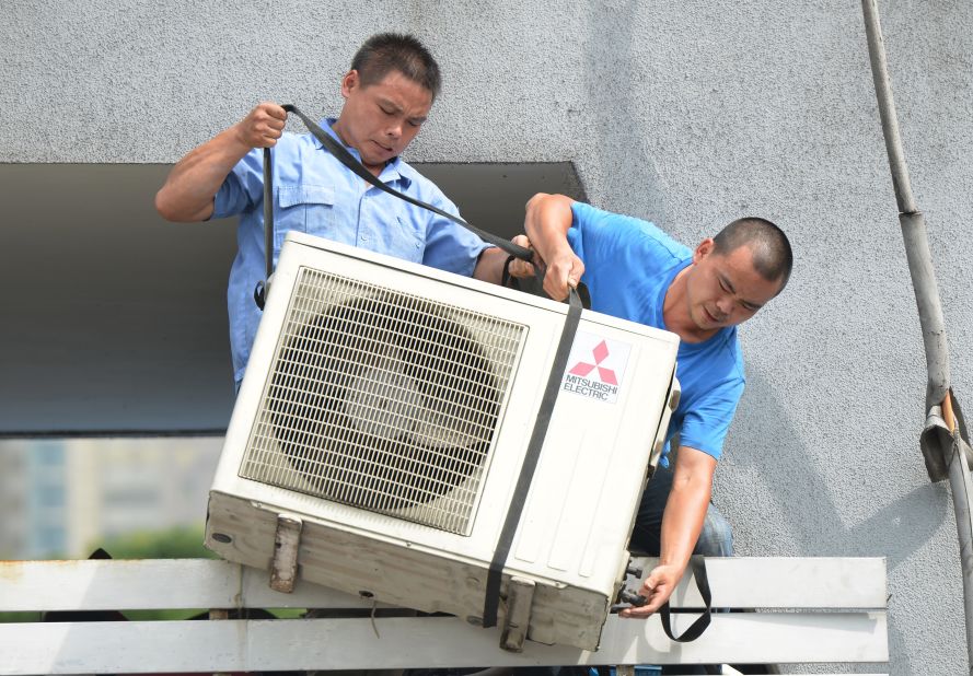 Workers install an air conditioning unit in a food stall in Shanghai on July 2.
