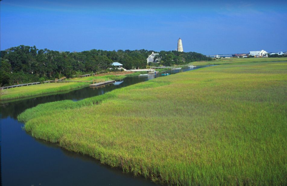 Bald Head Island is the southernmost of North Carolina's cape islands. Most of its 12,000 acres is set aside as natural preserves. The island includes the salt marsh and paddle trail, with the historic Old Baldy lighthouse and the beach shown in the distance.
