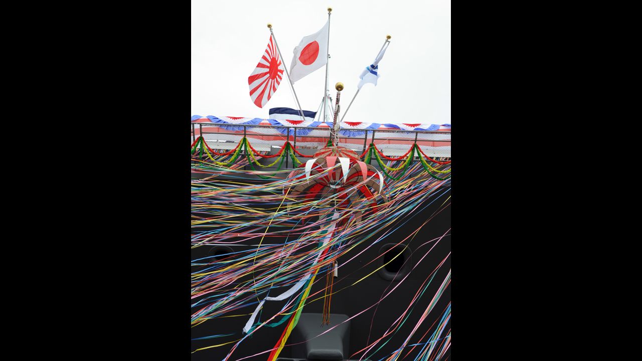 Japan's national flag, center, is displayed next to the flag for Japan's Maritime Self-Defense Force, left, above decorations streaming from the ship.