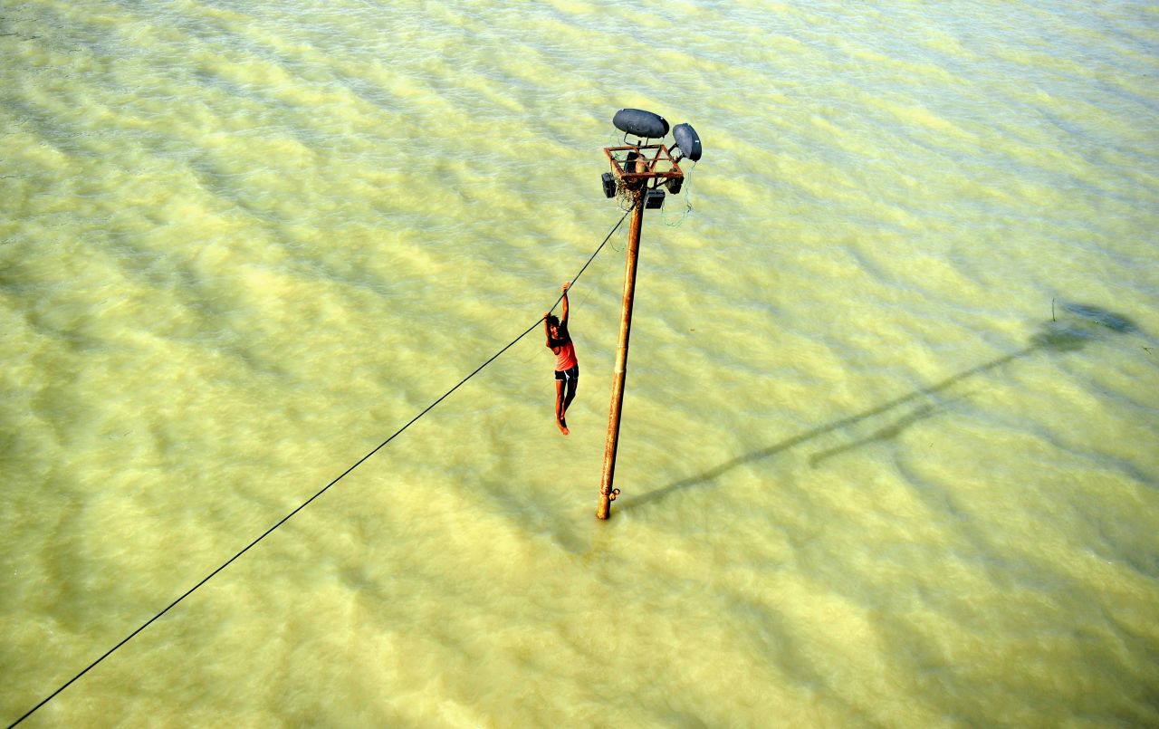 A person dangles from a power line before diving into the Ganges River in Allahabad, India, on Tuesday, August 6, after heavy monsoon rains. 